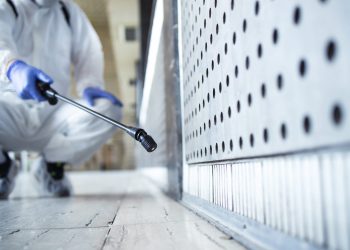 Unrecognizable person in white chemical protection suit doing disinfection of public areas to stop spreading highly contagious corona virus.